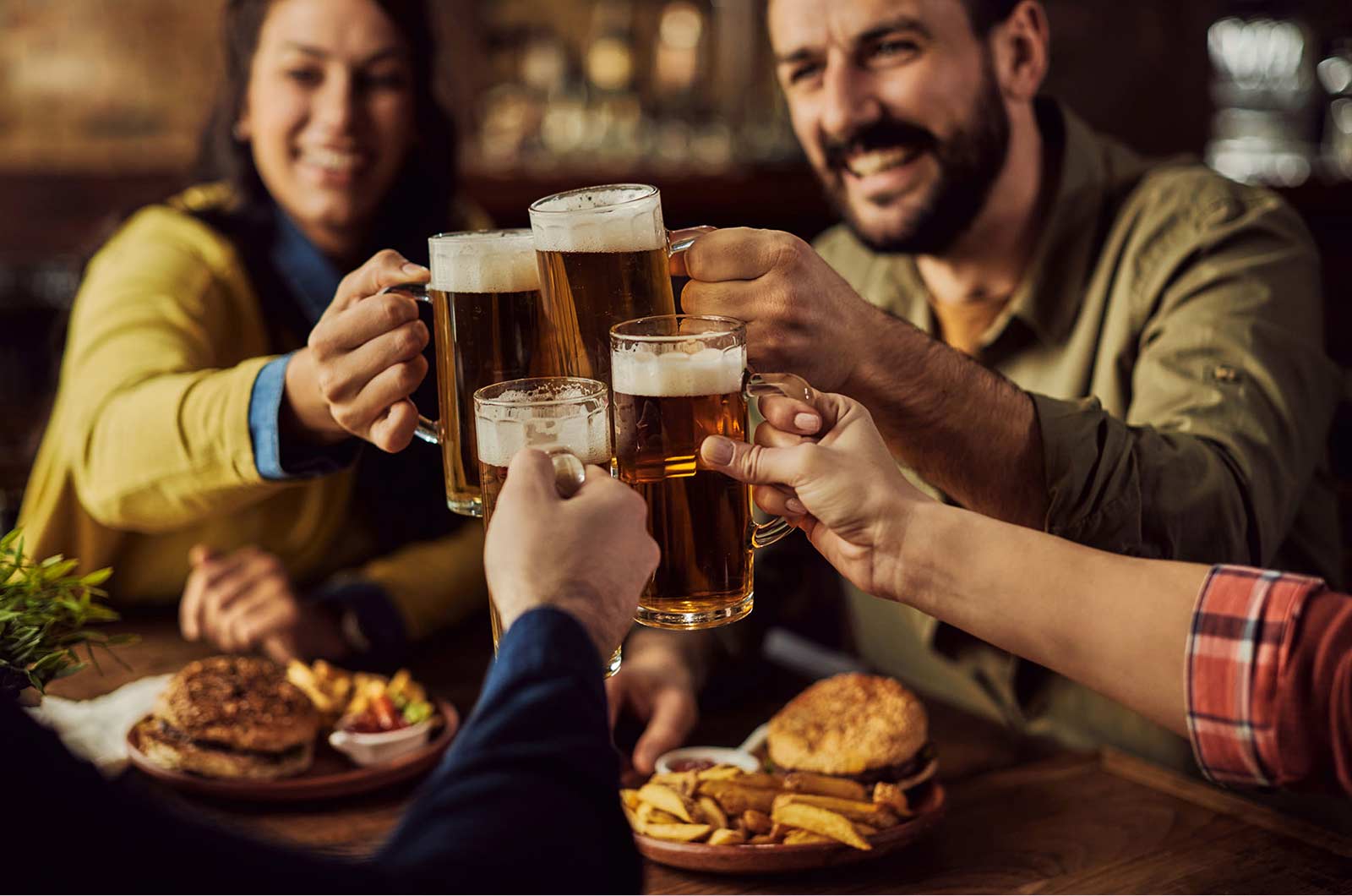 Close-up of group of friends toasting with beer while eating in a pub