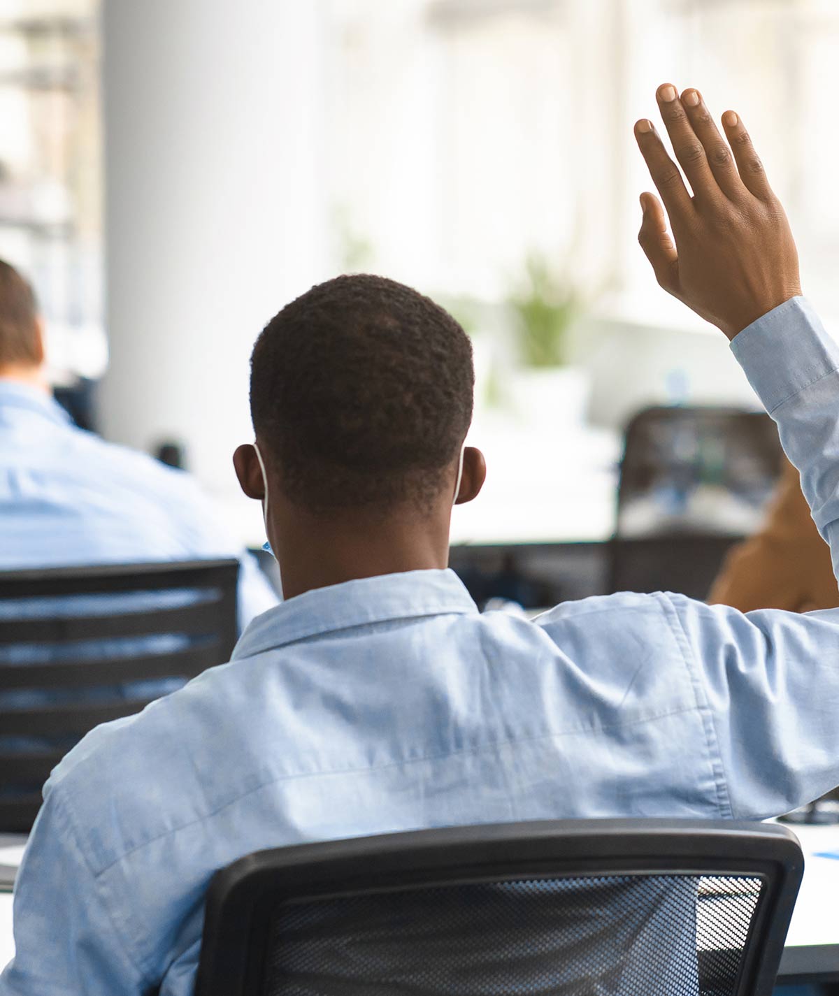 Rear back view portrait of african american guy student raising hand for answer or asking question, sitting at desk