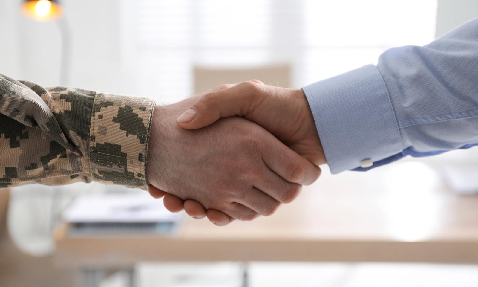 Soldier and businessman shaking hands indoors, closeup